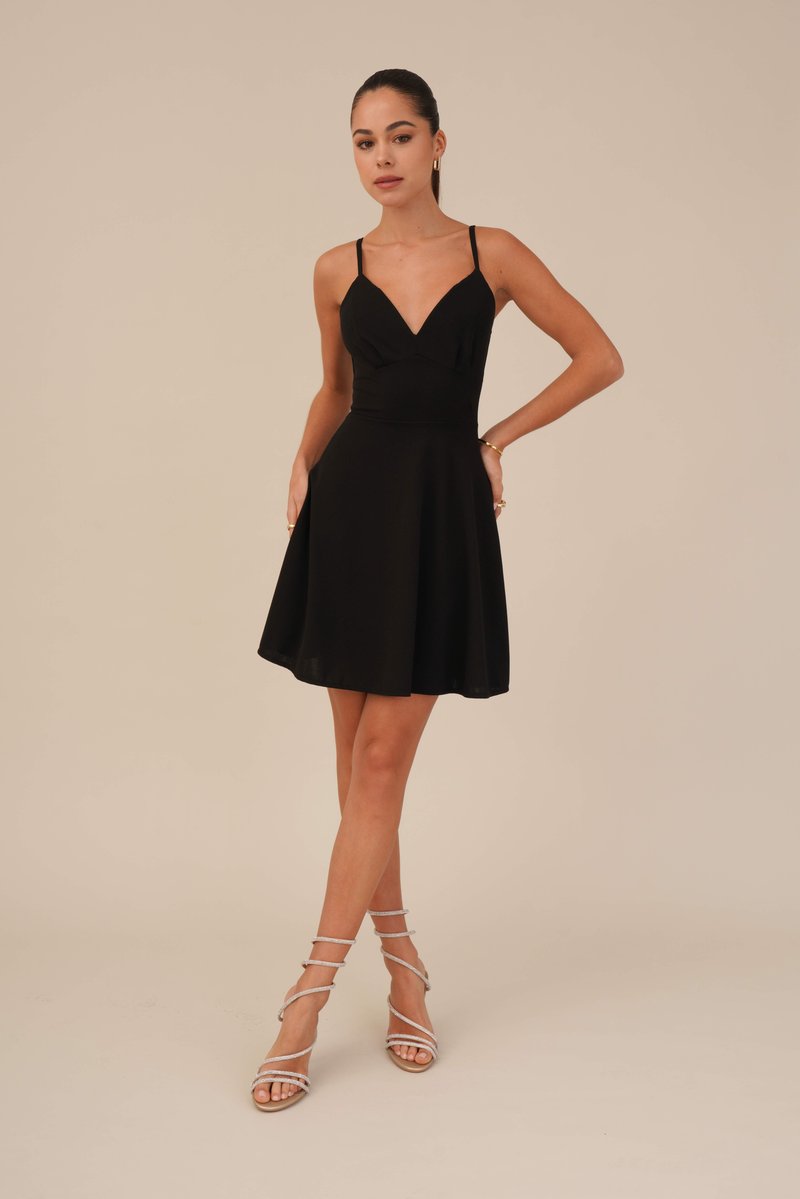 Schwarzes ärmelloses Kleid mit tiefem V-Ausschnitt, ausgestelltem Rock, Seitentaschen, aus glattem Stoff, kombiniert mit silbernen Riemchensandalen.