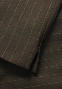 Brązowa tkanina w jodełkę z delikatnymi jasnoszarymi paskami, charakteryzująca się teksturowanym splotem i eleganckim wykończeniem. Widoczny szczegół złożonego brzegu.