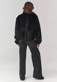 Czarna kurtka z sztucznego futra o luźnym kroju, z długimi rękawami. W połączeniu z czarnymi spodniami z wysokim stanem i szerokimi nogawkami.