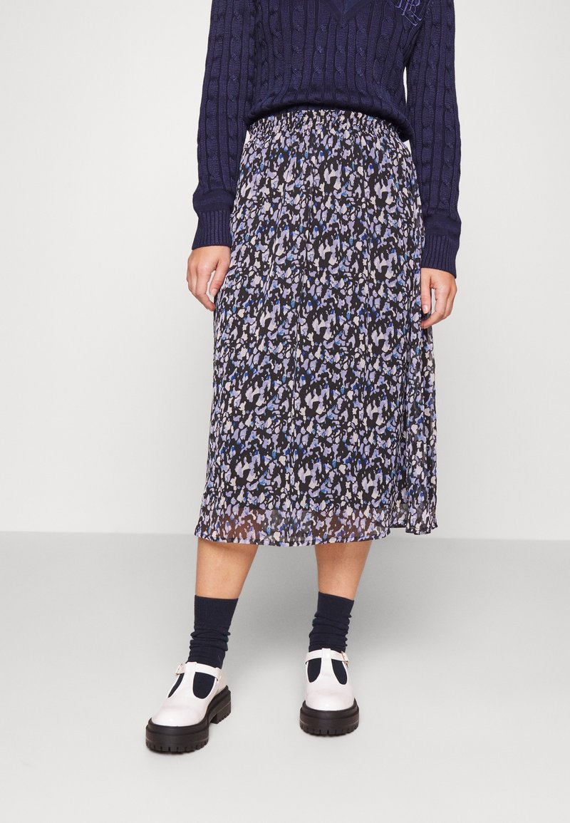 Floral pleated midi skirt in navy, purple, and white. Lightweight material, elastic waistband, with a flowy design. Worn with white shoes.