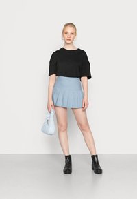 T-shirt oversized preto, saia mini plissada azul clara, botas de tornozelo pretas e uma pequena bolsa azul clara com uma alça atada.