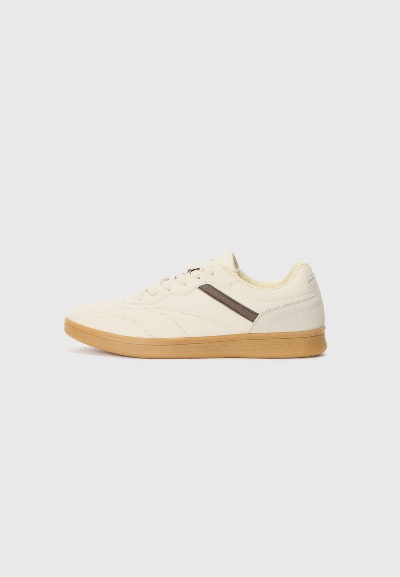 Basket en crème avec une tige texturée, une bande d'accent brun et une semelle en caoutchouc beige, présentant un profil bas et un design à lacets.