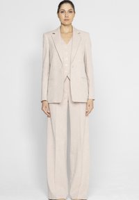 Jasnoróżowy lniany garnitur składający się z dopasowanej marynarki, kamizelki z błyszczącymi guzikami oraz szerokich spodni, z teksturowanej tkaniny.