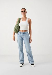 Light blue straight-leg jeans, white ribbed tank top, green quilted shoulder bag, and black-and-white sneakers. Accessories include sunglasses.