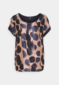 T-shirt z krótkim rękawem w kolorze brzoskwiniowym z granatowymi, abstrakcyjnymi kropkami. Miękka tkanina o gładkiej fakturze i luźnym kroju. Okrągły dekolt i kieszeń w szwie bocznym.