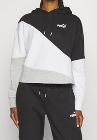 Hoodie med svarta, vita och grå paneler, tillverkad av mjukt material. Ikonisk Puma-logotyp på bröstet och detalj på sidofickan.