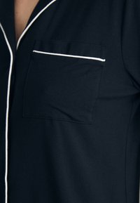 Chemise de pyjama bleu marine avec un col à piping blanc et une poche poitrine. Fabriquée dans un tissu doux avec une texture lisse.