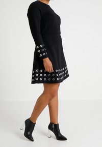 Musta mekko pitkillä hihoilla, jossa on hopeiset rei'itykset hihoissa ja helmassa. Sujuva pinta, istuva yläosa ja levenevä hame. Yhdistetty mustiin nilkkureihin.