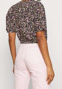 Blouse noire à motifs floraux avec manches courtes bouffantes, taille froncée, et pantalon rose taille haute avec poches arrière. Tissu en coton texturé.
