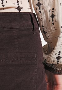 Braune Cordhosen mit hoher Taille und Seitentaschen, kombiniert mit einer leichten, gemusterten Bluse mit luftigen Ärmeln.