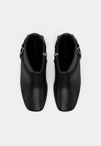 Mustad mustad, mis on valmistatud siledast materjalist, ümarate varvastega, külgsuunas kinnitatud buckliga ja madala kontsaga, mille saab jalga libistada.