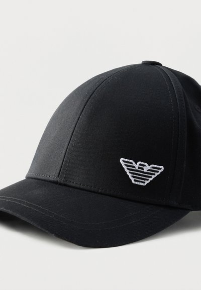 Μαύρο καπέλο μπέιζμπολ με κυρτό γείσο και λευκό κεντητό στυλιζαρισμένο λογότυπο αετού στο μπροστινό πάνελ, με φόντο ένα απλό ανοιχτό χρώμα.