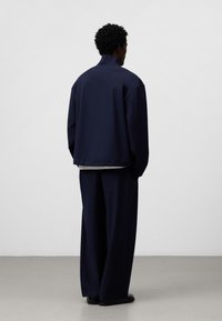 Marinblå oversized jacka med hög krage, parat med matchande vida byxor. Tillverkad av ett glatt, lätt tyg.