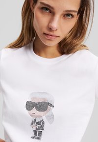 Bílý bavlněný tričko s designem kreslené postavičky ozdobené rhinestony. Postavička má na sobě sluneční brýle a oblek.