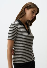 Polo a righe con maniche corte in bianco e nero, dotato di scollo a V e collo nero. Il tessuto sembra strutturato e presenta una forma aderente.