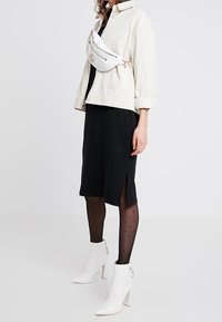 Valkoinen corduroy-takki, musta polvenpituinen mekko, pilkku sukkahousut ja valkoiset nilkkurit, joissa on lohkokorko. Valkoinen olkalaukku vetoketjuilla.