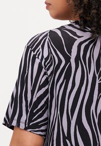 Fekete és levendula csíkos, rövid ujjú póló, puha tapintással és zebra-szerű mintával, vállról nézve.