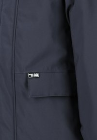 Navyblauwe geïsoleerde jas met een gladde textuur. Bevat een vierkante zak en een logotag met de tekst "READY SET GO."