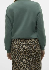 Vihreä pitkähihaisen puuvillainen collegepaita; yhdistettynä ruskeaan leopardi-kuvioiseen hameeseen, jossa on taskut ja näkyvät ompelusaumat.