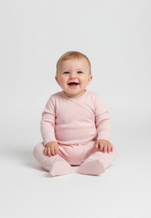 Smilende baby med lyst hår, der sidder på en hvid overflade og bærer en lyserød heldragt med fødder.