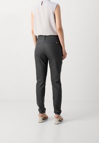 Gray slim-fit trousers with a smooth texture, featuring a small logo on the back pocket. Paired with a light-colored sleeveless top.