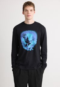Tricou negru cu mânecă lungă, având un grafic cu un vultur în nuanțe de albastru și negru, cu numele mărcii "HUGO" afişat sub design.