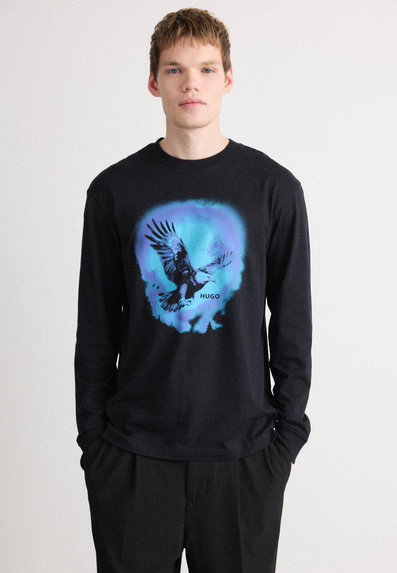 Tricou negru cu mânecă lungă, având un grafic cu un vultur în nuanțe de albastru și negru, cu numele mărcii "HUGO" afişat sub design.