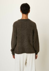 Pull en peluche marron foncé avec un col rond et des manches longues. Présente une coupe décontractée, une finition côtelée et une texture douce.