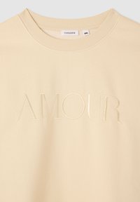 Felpa beige con la parola ricamata "AMOUR" in una tonalità leggermente più chiara, con un classico scollo rotondo e polsini a costine.