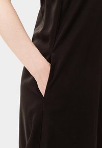 Sort kjole med en side lomme. Stoffet ser glat og let skinnende ud, med et tætsiddende design, der omfavner kroppens konturer.