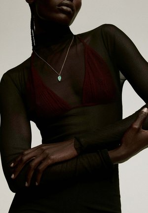 Prenda negra transparente de manga larga superpuesta sobre un sujetador burdeos oscuro. Presenta un delicado collar de plata con detalles de charm en turquesa.