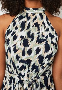 Šaty bez rukávů s halter výstřihem v námořnické modré, krémové a zelené abstraktní potisku. Mají nařasenou látku a zavázaný pas pro nastavitelné padnutí.