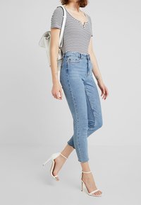 Haut à manches courtes rayé avec un col rond, associé à un jean taille haute bleu clair et des talons blancs à lanières. Les accessoires comprennent un sac à dos blanc.