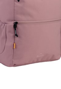 Sac à dos rose clair avec une surface texturée, présentant des fermetures éclair noires et une étiquette d'accent orange. Logo en relief sur le côté.