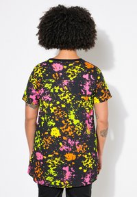 Camiseta negra con patrones de salpicaduras vibrantes en rosa, naranja, verde neón y amarillo. Manga corta y diseño de dobladillo redondeado.