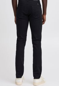 Zwarte denim jeans met een slim fit, voorzien van twee achterzakken met een subtiel ontwerp, en gecombineerd met crèmekleurige sneakers.