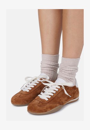 Pruunist sametist tennisjalanõud valgete detailidega, ribatud beežid sokid ja paeltega disain. Omab tekstuurset pinnaset ja ümarat varvaste kuju.