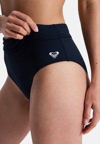 Schwarze Badehose mit hohem Bund aus glattem Stoff; verfügt über ein kleines weißes Herzlogo an der Seite und einen robusten Bund.