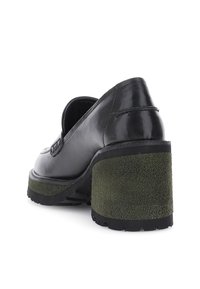 Mocassino in pelle nera con tacco a blocco testurizzato di un verde scuro e suola in gomma, mostrato da un angolo posteriore basso su uno sfondo bianco.