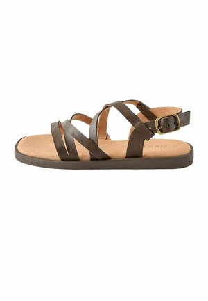 Brown flat sandal with three crisscross leather straps, back strap with a brass buckle, and a cushioned tan footbed.