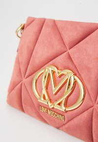 Pochette in suede trapuntato rosa con hardware dorato e dettagli del logo in evidenza. Presenta una texture liscia e un motivo geometrico.