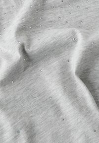 Tessuto grigio con una consistenza morbida, caratterizzato da scintillanti strass distribuiti su tutta la superficie.