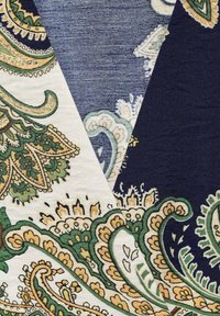 Tissu multicolore présentant des motifs paisley complexes en vert, jaune et bleu marine, avec une surface texturée et des sections contrastées.