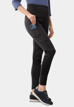 Zwarte legging met een hoge taille en zijzak, gemaakt van rekbare stof. Geweven naden lopen langs de zijkanten, gecombineerd met donkere sportschoenen.