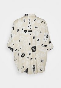 Chemise beige à manches courtes avec motifs floraux et de vase abstraits en noir et blanc, vue de dos sur fond blanc.