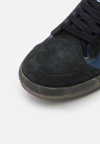 Black sneaker with a textured suede toe, mesh upper, and blue accents. Features black laces and a rubber sole with a slight sheen.