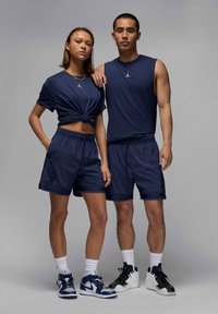 Completo sportivo navy composto da una maglietta a maniche corte con nodo e pantaloni corti con cintura elastica. Dettagli significativi: accenti di logo bianchi e calzature in contrasto.