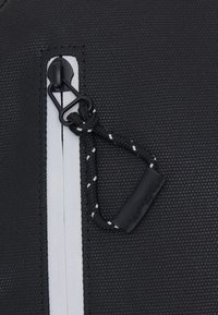 Zwarte textielmateriaal met een gestructureerd oppervlak, voorzien van een ritsluiting en een gedetailleerde ritsenhouder met zwart-witte accenten.