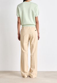 Light green short-sleeve sweater with a ribbed hem paired with beige high-waisted trousers featuring side pockets and subtle pleating.