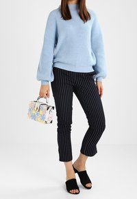 Jasnoniebieski sweter z prążkowanej tkaniny z balonowymi rękawami, czarne spodnie do kostek w paski, czarne klapki oraz torebka w kwiatowy wzór.